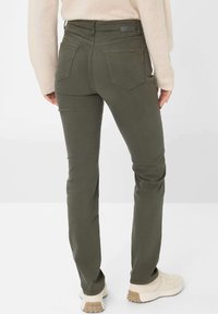 Olivgrüne Jeans mit schlanker Passform, Gesäßtaschen und strukturiertem Stoff. Kombiniert mit hellen Sneakers. Einfaches Design des Hosenbunds.