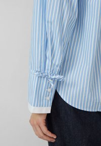 Blauw-witte gestreepte shirt met een manchet vastgebonden om de pols en knoopdetails, gemaakt van lichtgewicht stof, met een gebogen zoom.