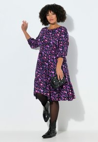 Fioletowa sukienka w kwiaty z rękawami do łokcia i rozkloszowanym dołem, zestawiona z czarnymi, ćwiekowanymi botkami za kostkę oraz małą czarną torebką.