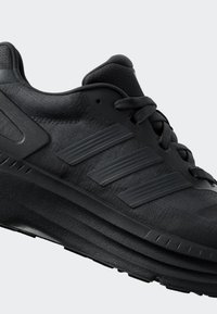 Černá sportovní bota s texturovaným svrškem, třemi horizontálními pruhy a silnou, vrstvenou podrážkou. Šňůrky a očka jsou také černé.