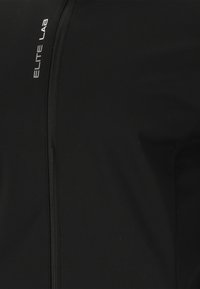 Veste de sport noire avec fermeture éclair, texture lisse et logo discret en blanc sur le côté gauche. Coupe ajustée pour la performance.