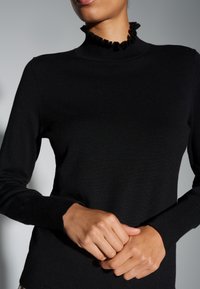 Haut en maille noire à manches longues, doté d'un col montant froufroutant. Texture lisse, coupe ajustée et poignets côtelés.