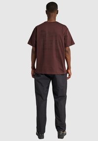 Brun bomull t-shirt med korta ärmar, pryds av fet svart text tryckt på baksidan, matchad med lösa svarta byxor och skor.