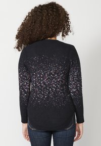 Pulover negru cu un model texturat, pistruiat în nuanțe de albastru, roșu și alb, având mâneci lungi și un tiv rotund.