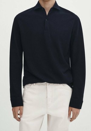 Navy long-sleeve polo shirt made of soft fabric, featuring a traditional collar, three-button placket, and ribbed cuffs. Paired with light pants.
