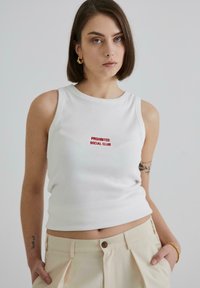 Hvid ribbet tanktop med rød broderet tekst "PROHIBITED SOCIAL CLUB" i midten. Kombineret med lyse beige bukser.