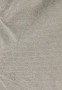 Ljust grått texturerat tyg med en något veckad yta, som har ett subtilt vävt mönster med en präglad cirkulär logotypdetalj.