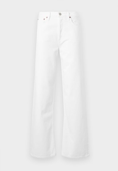 Άσπρο τζιν με ψηλή μέση και φαρδιά μπάτζια, με κούμπωμα κουμπιού και φερμουάρ μπροστά και πεντάτσεπη σχεδίαση σε ανοιχτό γκρι φόντο.