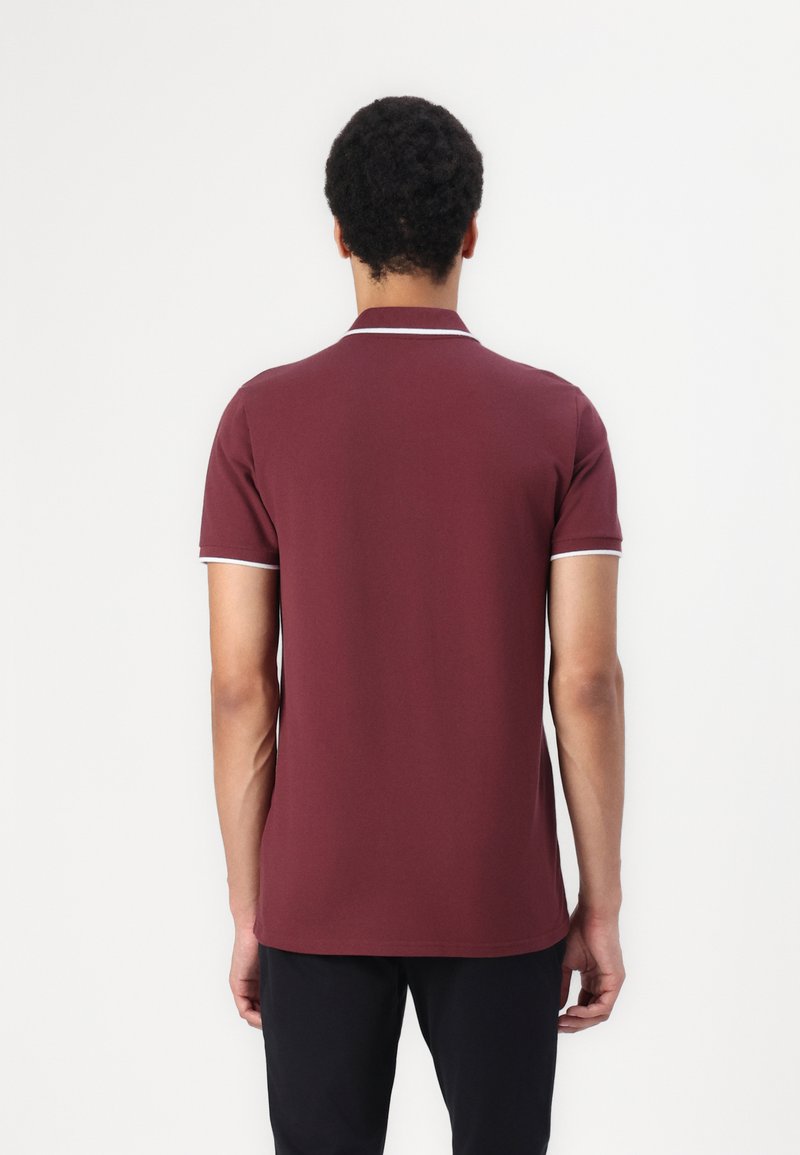 Polo en bordeaux avec col et manches courtes, présentant une finition blanche le long du col et des bords des manches, fabriqué en tissu lisse.