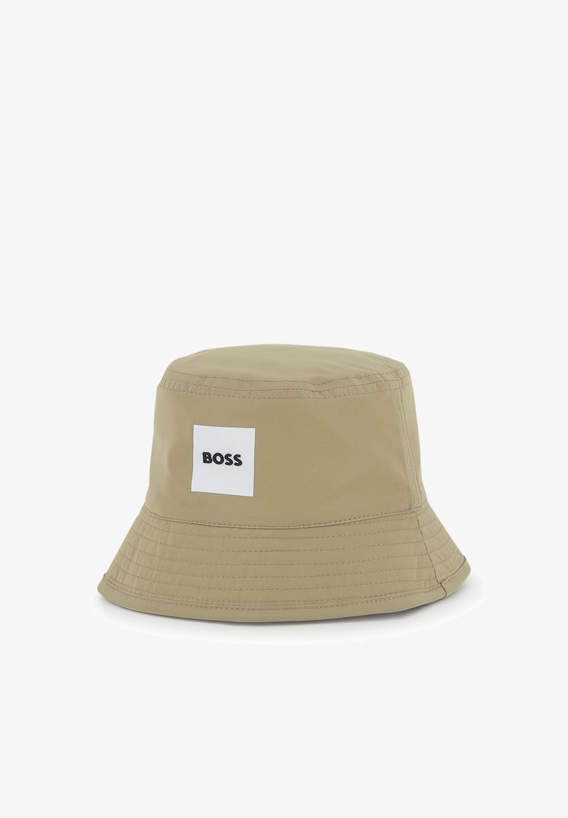 Chapeau bob beige en tissu lisse, avec un patch carré blanc portant le logo "BOSS", une visière structurée et des détails de couture autour du bord.
