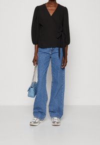 Sort indpakningsbluse med puffærmer, blå høj-midte flare jeans, grå sneakers og en lille blå håndtaske med kædestropper.