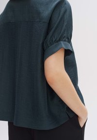 Maglietta a maniche corte color verde scuro, con finitura testurizzata, polsini arrotolati e orlo arrotondato, progettata per un fit rilassato.