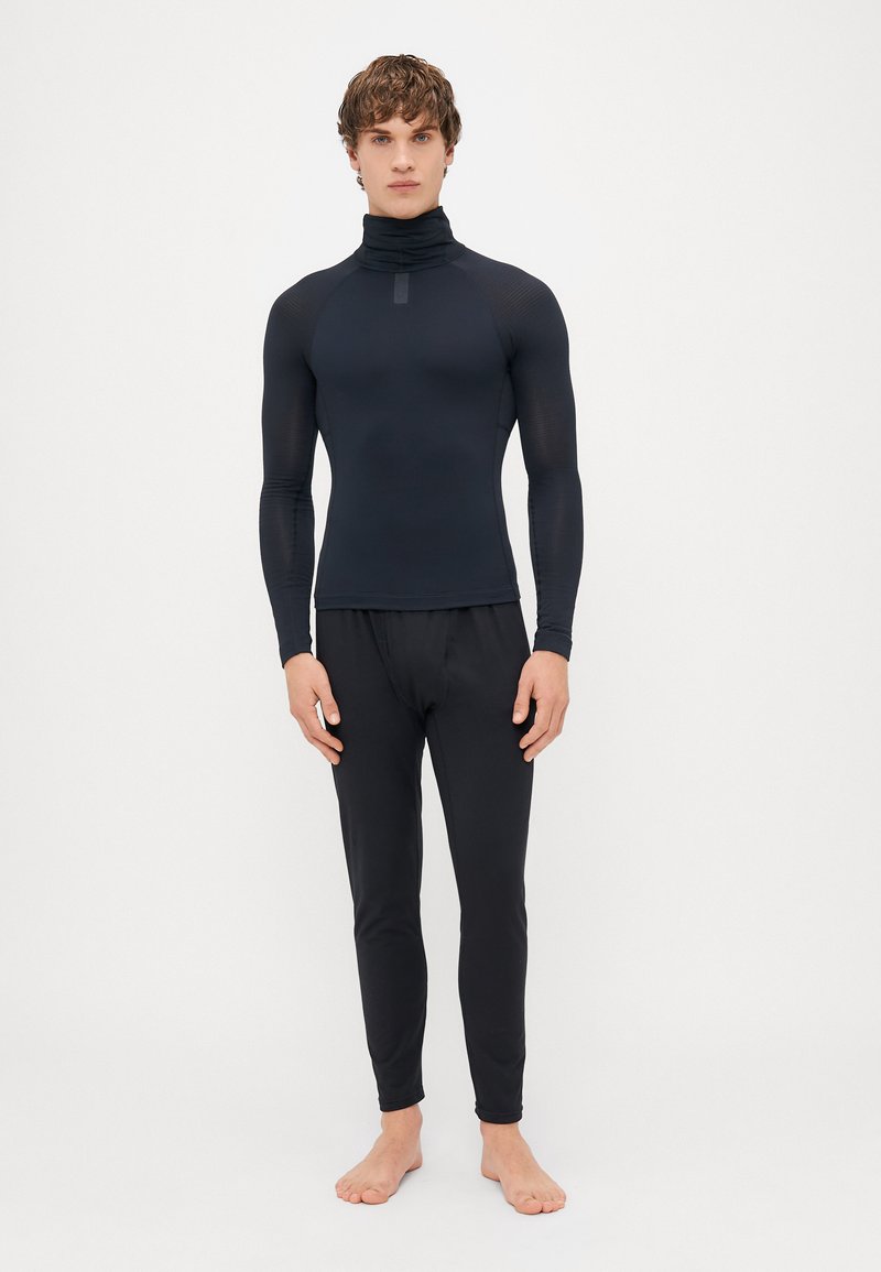 Zwart aansluitend long-sleeve shirt met hoge hals en geribbelde textuur, gecombineerd met bijpassende slim-fit broeken voor een gecoördineerde look.