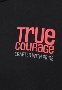 Fekete póló merész piros és szürke grafikai szöveggel: "IGAZI BÁTORSÁG" és "BÜSZKÉN KÉSZÍTVE" modern betűtípussal. Puha pamut anyag.