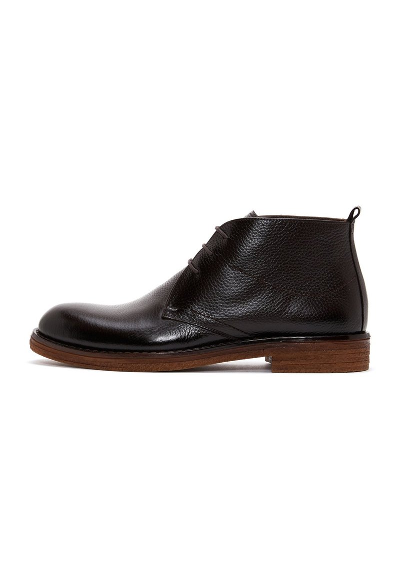 Bottine en cuir noir avec une finition texturée, bout rond, trois trous pour les lacets et une semelle en bois brun. Elle comprend une petite languette à l'arrière.