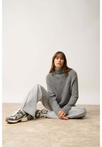 Szary sweter dziany z wysokim kołnierzem i diamentowymi wzorami, zestawiony z szerokimi, jasnoszarymi dżinsami oraz szarymi trampkami z ciemną podeszwą.