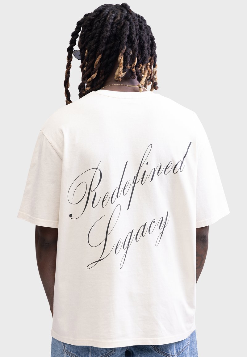Cremiger Baumwoll-T-Shirt mit lässigem Schnitt, auf dem Rücken mit elegantem schwarzen Schriftzug "Redefined Legacy" bedruckt.