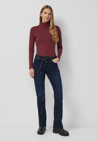 Bordowy golf w połączeniu z ciemnoniebieskimi dżinsami ozdobionymi detalem z łańcuszkiem. Dżinsy mają prosty krój nogawek i przednie kieszenie.