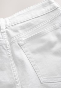 Gros plan sur la zone de la poche arrière d'un jean en denim blanc montrant les détails des coutures et une passants de ceinture.