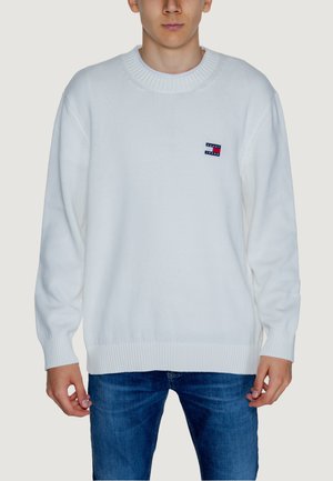 Maglione bianco lavorato a maglia con polsini e orlo a coste. Presenta una piccola toppa con logo blu, rosso e bianco sul lato sinistro del petto. Vestibilità ampia.
