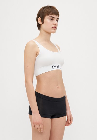 Bijela rebrasta bralette s mornarskom "POLO" trakom, uparen s crnim prilagođenim šortsem. Materijali izgledaju mekano i rastezljivo.
