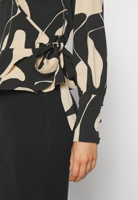 Langärmliges Oberteil in Schwarz mit einem cremefarbenen abstrakten Muster, mit einem gebundenen Bund und geknöpften Manschetten, kombiniert mit einem gerippten schwarzen Rock.