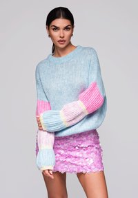 Maglione lavorato a maglia blu chiaro con maniche a righe rosa e gialle, abbinato a una gonna a tubino rosa con paillettes. Tessuto liscio, vestibilità comoda.