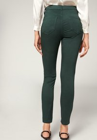 Pantalones estilo legging de talle alto en verde, con una textura suave, que cuentan con dos bolsillos en la parte posterior y una silueta ajustada.