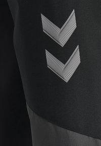 Leggings atletici neri con una texture liscia, dotati di un pannello grigio a contrasto e tre motivi a chevron in argento su un lato.