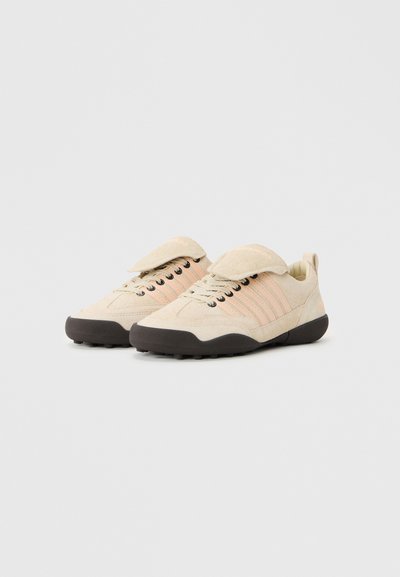 Chaussures en daim beige avec une finition texturée, dotées d'une languette repliable, de rayures roses et de semelles en caoutchouc noir pour une bonne adhérence.