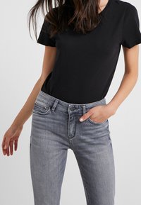 Camiseta de algodón negra combinada con jeans de denim gris. Los jeans tienen un corte clásico con bolsillos y cierre de botón. Textura suave.