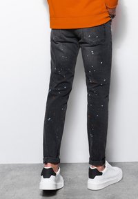 Harmaat denimfarkut, joissa oranssin ja valkoisen maalisplatterointi, slim fit -leikkaus, käännetyt lahkeet ja tavanomainen viiden taskun malli. Yhdistetty valkoisiin lenkkareihin.