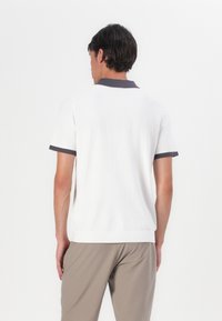 Λευκό κοντομάνικο πόλο μπλουζάκι με αντίθετους σκούρους γκρι γιακά και μανίκια, με απαλό υφή και άνετη εφαρμογή.