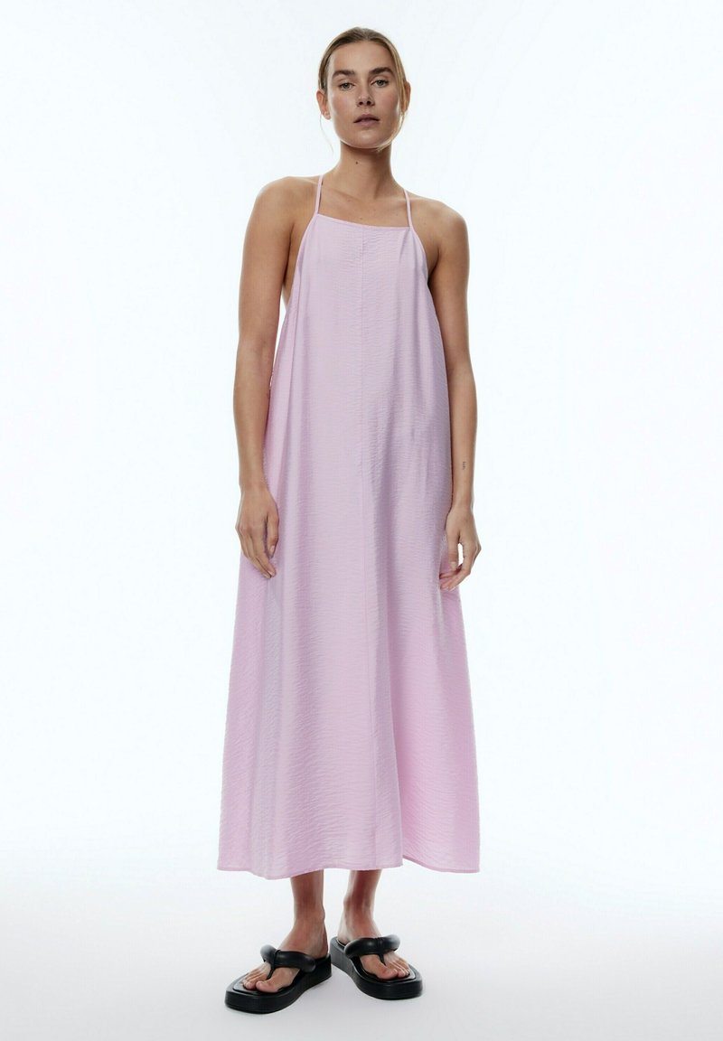 Langes, hellrosa Kleid aus gekräuseltem Stoff, mit einem Neckholder-Design und einer lockeren Passform, die bis zur Mitte der Wade reicht, kombiniert mit schwarzen Sandalen.