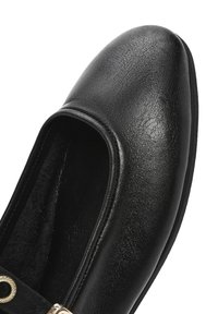 Zapato de cuero negro con puntera redondeada, textura suave y una correa decorativa con un detalle de metal dorado. El interior parece suave.