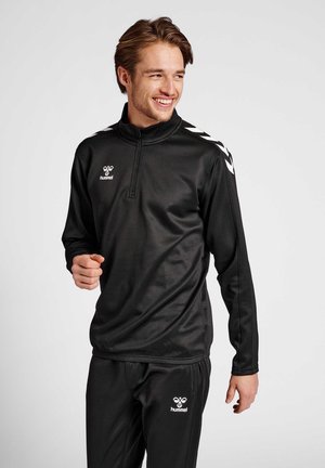 Schwarzes Sportbekleidungsset mit einem langärmeligen Oberteil mit Reißverschluss und passenden Hosen. Das Material ist glatt und hat weiße Logos und Schulterakzente.