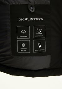 Zwarte jas met een label met verzorgingsinstructies en materiaaldetails. Toont iconen voor 2-laags stof, waterafstotend en isolatie.