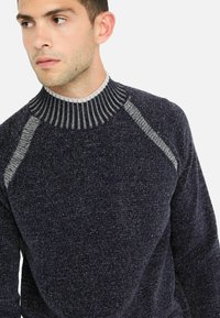Pulover tricotat bleumarin cu un guler rotund ribflat și un material texturat, având accente gri deschis pe umeri și guler.