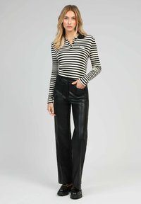 Polo shirt à rayures noires et blanches à manches longues avec col, associé à un pantalon en cuir noir taille haute et des chaussures noires imposantes.