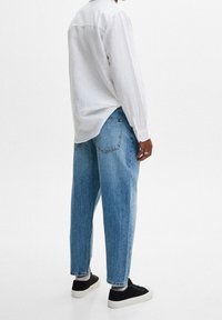 Vit långärmad skjorta, denimblå baggy jeans, svarta sneakers. Skjortan är något oversized med en mjuk textur; jeansen har en klassisk passform.