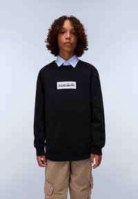 Felpa nera con maniche lunghe, scollatura rotonda e patch del logo sul petto, abbinata a una camicia colletto azzurro chiaro. Pantaloni cargo color sabbia.