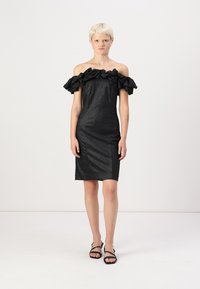 Μαύρο φόρεμα κάτω από τους ώμους με ροζέτα στον λαιμό, εφαρμοστό σχέδιο, γυαλιστερή υφή, μήκος μέχρι το γόνατο, συνδυασμένο με μαύρες σανδάλες με λουριά.