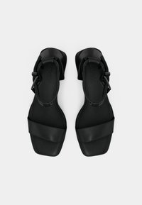 Schwarze flache Sandalen mit einer glatten, matten Oberfläche, zwei breiten Riemen über dem Fuß und einem Schnallenverschluss am Knöchel. Rechteckige Zehenpartie.