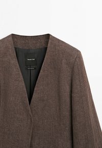 Bruine blazer met textuur, V-hals en zwarte binnenvoering, gelabeld Massimo Dutti, gemaakt in Portugal, gepresenteerd op een witte achtergrond.