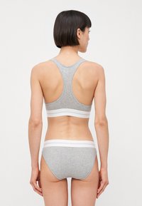 Top sportivo grigio con design a racerback e una fascia elastica bianca. Accompagnato da slip bikini grigi abbinati con una vita bianca.