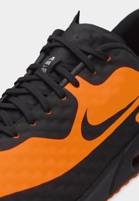 Chaussure de sport Nike noire et orange avec des lacets noirs et une unité de semelle Air Max visible.