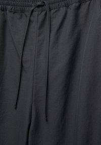 Zwarte broek met trekkoord van zacht materiaal. Voorzien van een elastische tailleband en een gladde structuur. Subtiele stikseldetails nabij de tailleband.
