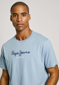 Šviesiai mėlynas trumpomis rankovėmis medvilninis marškinėliai su tamsiai mėlynu "Pepe Jeans" logotipu ir tekstu "LONDON". Klasikinė apvalios iškirptės forma ir švelni tekstūra.
