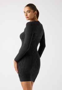 Abito a maglia nero aderente con maniche lunghe, un motivo a trecce testurizzato e orlo a coste.