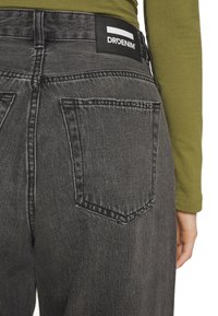 Jeans de ganga pretos de cintura alta com um acabamento texturizado, apresentando dois bolsos traseiros e uma etiqueta de tecido com a marca na cintura.